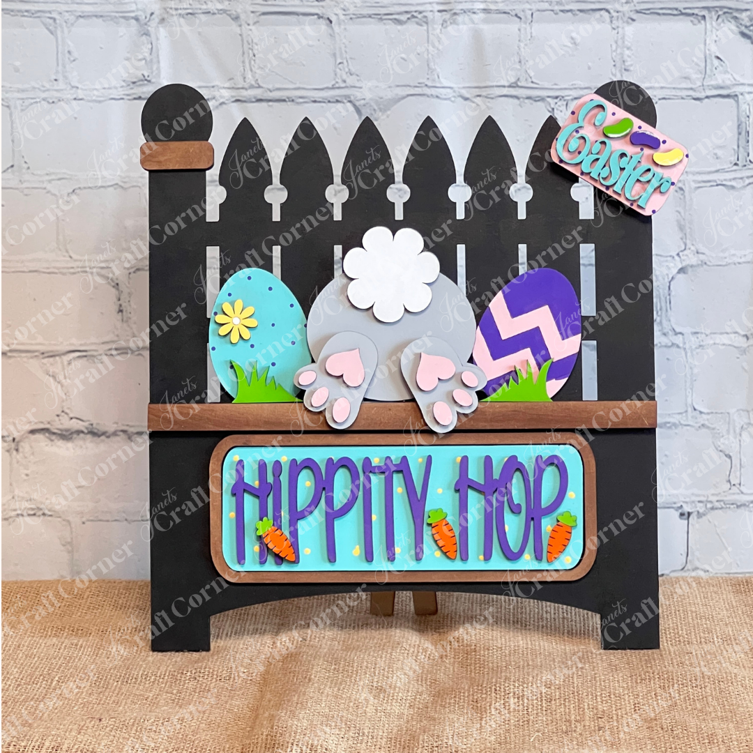 Janet's Craft Corner offers a charming DIY home decor kit featuring a bunny bottom, colorful eggs, a "Hippity Hop" sign with carrots, and an "Easter" tag on burlap. This Garden Fence with Insert includes a black picket fence and interchangeable inserts for endless creativity.