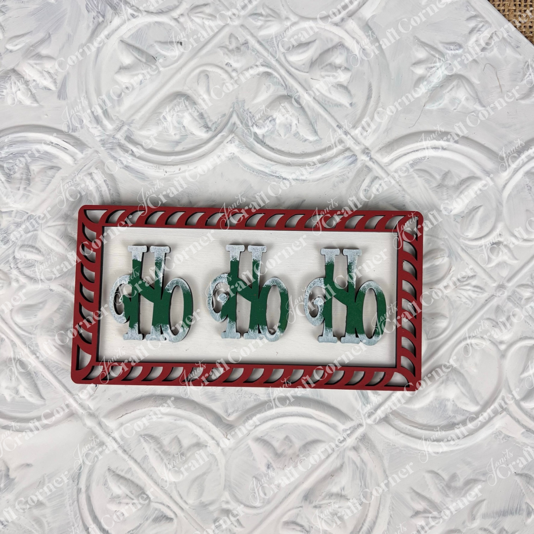 The Vintage Santa Cookies Decor Set DIY craft kit from Janet's Craft Corner features three green "Ho" letters with Santa hats inside a red and white striped frame—perfect for festive holiday decor or crafting at home.