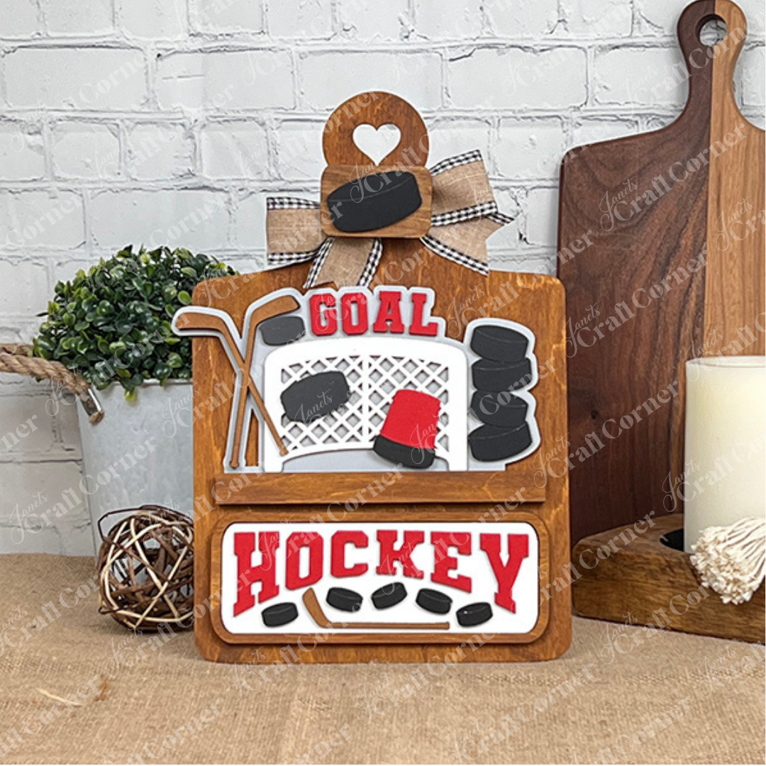 Janet's Craft Corner offers a Breadboard Interchangeable Base with Insert, a DIY kit featuring "GOAL" and "HOCKEY" on a decorative plaque with hockey motifs. It's perfect home decor, complete with a bow, and complements any space with accompanying items like a potted plant or candle.