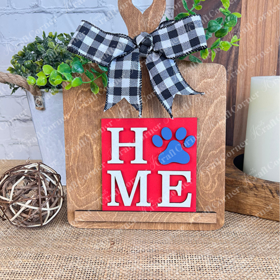 Janet's Craft Corner's Dog Squares features a wooden cutting board with a black and white checkered bow, red "HOME" sign with a blue paw print as the "O," perfect rustic decor for tiered trays or burlap displays.