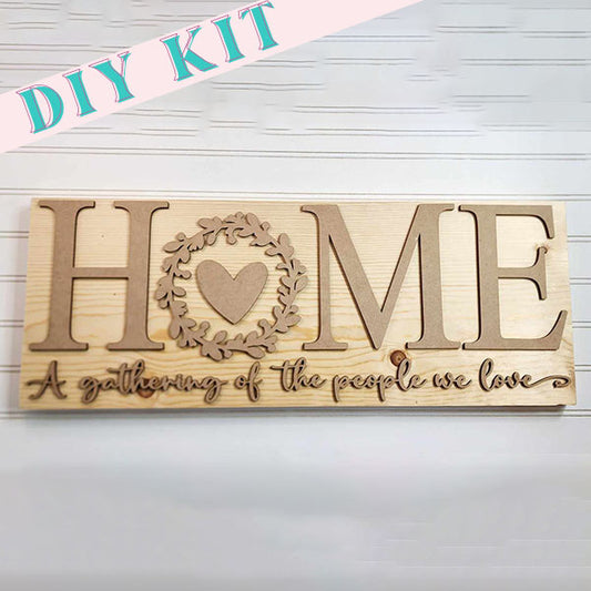 The Home Mantle Sign from Janet's Craft Corner includes a wooden sign that features the word "HOME" with a heart substituting for the "O," evoking farmhouse charm. Below, it states, "A gathering of the people we love." This is ideal for adding warmth to any cozy space with its light, textured background.