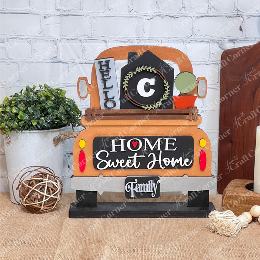 A Home Monogram Interchangeable Insert from Janet's Craft Corner, featuring phrases like "Home Sweet Home" and "Family" with a wreath and "Hello," sits decoratively on burlap against a brick wall.