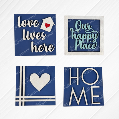 Add charm to any space with Janet's Craft Corner Home Squares—four decorative blue wood pieces for tiered trays: "love lives here" (house), "Our happy Place" (frame), heart with lines, and "HOME" with a heart-shaped "O".