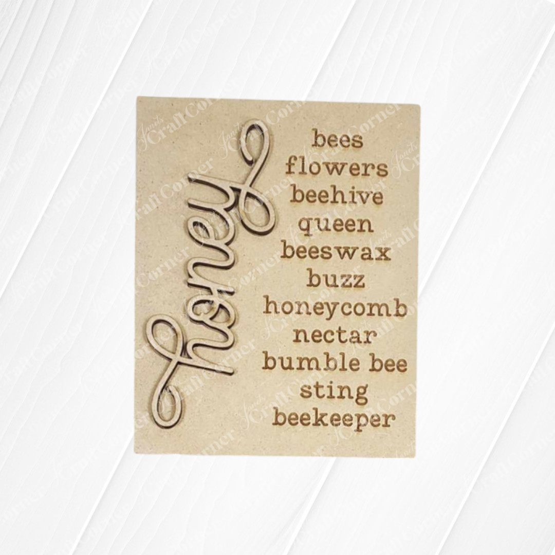 The raw wood DIY craft kit from Janet's Craft Corner features the word "honey" in decorative script and bee-related words like bees, flowers, and beehive. It's a perfect craft kit to add natural sweetness to your home decor.