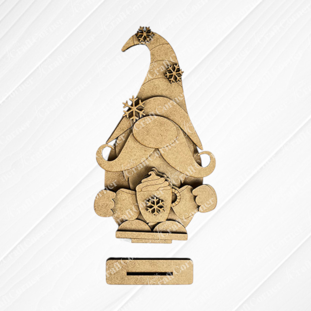 The Hot Cocoa Gnome from Janet's Craft Corner features a tall hat, bushy beard, and snowflake mug. This DIY shelf sitter kit offers seasonal home decor with a textured white diamond on a woven beige background.