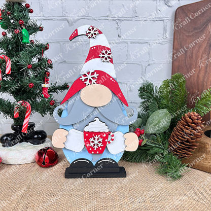 The Hot Cocoa Gnome from Janet's Craft Corner is a charming festive figurine holding a red mug of steaming hot cocoa, complete with a swirl of whipped cream. This delightful gnome features a tall hat adorned with snowflakes and is accompanied by a small decorated Christmas tree, ornaments, and pine cones on a rustic burlap surface—ideal for adding charm to your home decor.