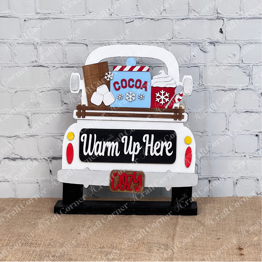 Janet's Craft Corner offers the Hot Cocoa Interchangeable Insert, a DIY seasonal home decor craft kit. This charming 3-piece set features a vintage truck with cocoa, marshmallows, and whipped cream against a white brick wall. It reads "Warm Up Here" with "Cozy" on the license plate—ideal for craft enthusiasts!.