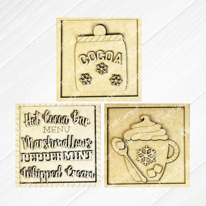 Janet's Craft Corner Hot Cocoa Squares are DIY decor kits with three laser-cut wooden pieces: a snowflake cocoa mug, a "Hot Cocoa Bar Menu" sign, and a steaming cup with whipped cream and snowflake details.