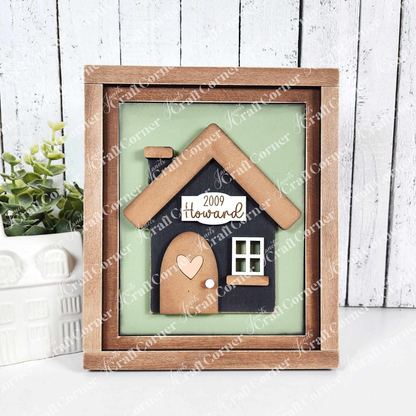 This sample of the charming DIY craft kit from Janet's Craft Corner features a farmhouse sign with a cozy house and heart door on a light green background. A plant and decor enhance the inviting scene in this House Interchangeable Farmhouse Sign set of 1.