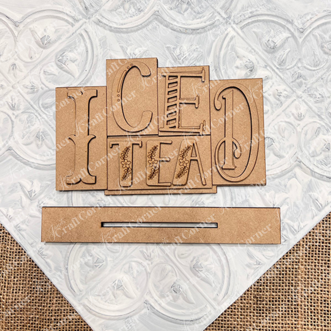 The Iced Tea Mini Word Block by Janet's Craft Corner features overlapping wooden letters spelling "Iced Tea" on a textured white and burlap base, perfect for home décor. A separate wooden strip is included, ideal for DIY seasonal home decor projects.