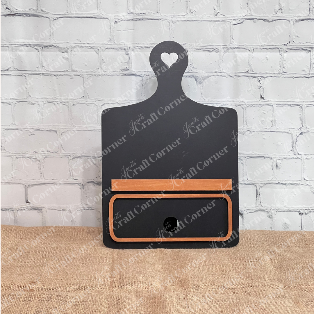 Janet's Craft Corner offers the Breadboard Classic Interchangeable Base with Insert DIY kit. This decorative white board has a heart handle,  stained face markings, and interchangeable accessories—ideal for DIY enthusiasts against a burlap backdrop.