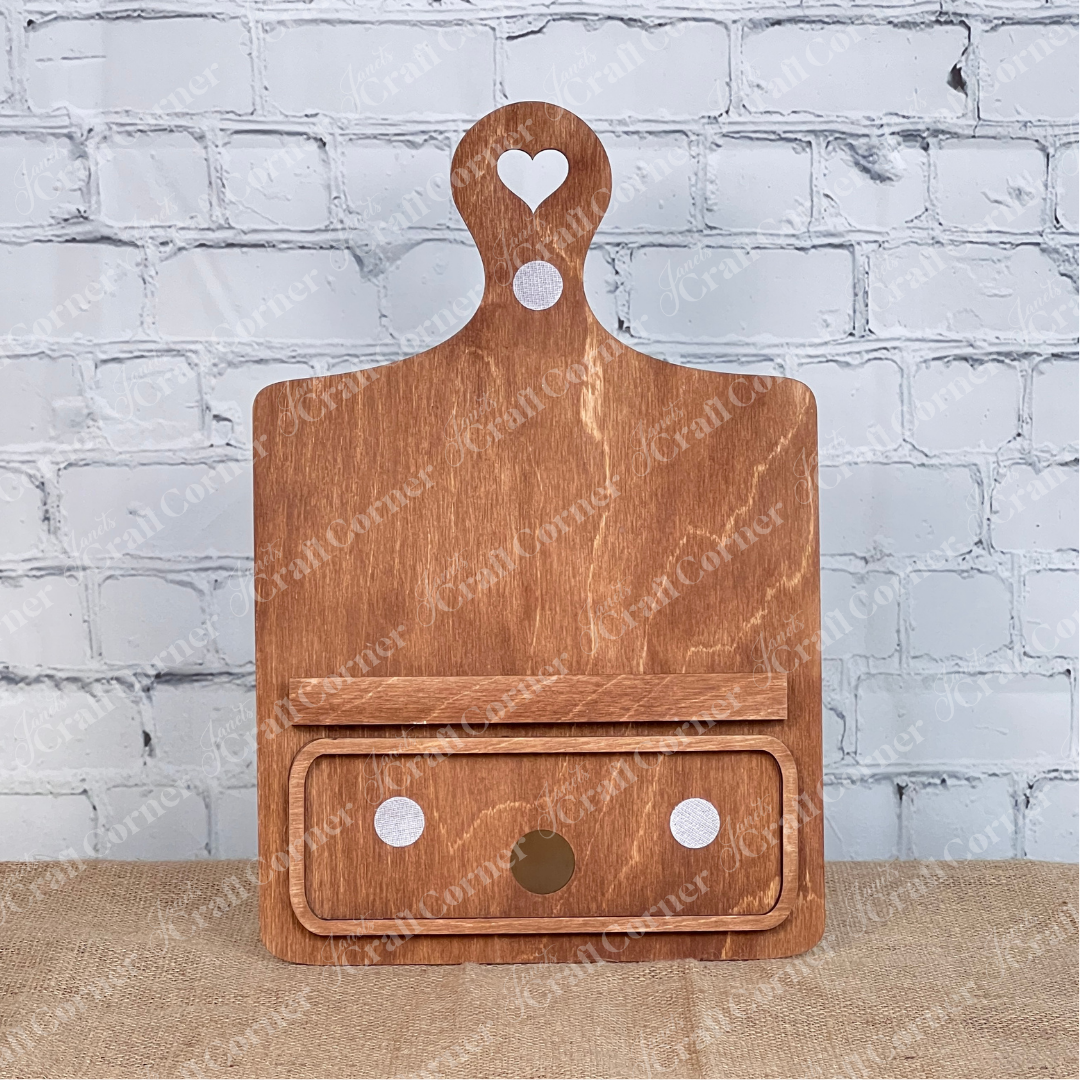 The Breadboard Classic Interchangeable Base by Janet's Craft Corner features a handle with a heart-shaped cutout and a built-in locations for the 3 pieces of a classic interchangeable insert, finished in natural wood. Ideal for home décor, it’s set against a white background, ideal as part of their DIY home decor kit.