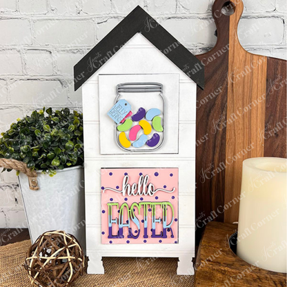 The Hello Easter Squares by Janet's Craft Corner features a house-shaped wooden sign with a jar of colorful jellybeans above a pink "hello EASTER" message—perfect spring decor for your home.