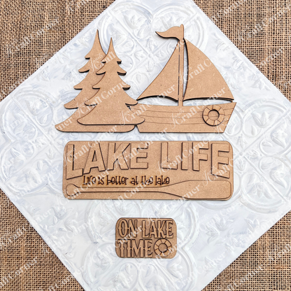 Janet's Craft Corner Lake Life Interchangeable Insert is a DIY craft kit featuring 3 wooden pieces—two pine trees, a sailboat, and two signs with "Lake Life" phrases—perfect for seasonal home decor.