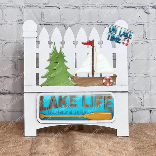 The Lake Life Interchangeable Insert by Janet's Craft Corner is a DIY seasonal home decor craft kit with 3 pieces, perfect for adding lake-themed charm to your space. Shown displayed on a white garden fence interchangeable base.