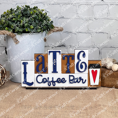 This charming home décor piece from Janet's Craft Corner, called the Latte Mini Word Block, displays "Latte Coffee Bar" in blue and black on a white background. It includes a delightful coffee cup illustration with a red heart, making it perfect for coffee lovers and adding warmth to any space when displayed against its white brick wall setting.