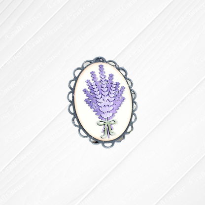 The Lavender Decor Set by Janet's Craft Corner features an oval brooch with purple lavender flowers and a green ribbon on a white background with a silver border—ideal for DIY projects or as an accent for your lavender mini sign.
