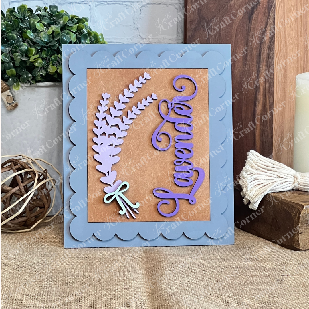 The Lavender Switchable Farmhouse Signs DIY Craft Kit by Janet's Craft Corner features a handmade card with a scalloped blue frame, lavender sprigs, "Lavender" in purple script, and rustic greenery—perfect farmhouse décor or sign inspiration.