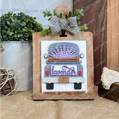 The Lavender Switchable Farmhouse Signs – DIY Craft Kit by Janet's Craft Corner features a vintage truck with lavender flowers, clipped to a wooden board with a striped bow, perfect for adding rustic charm to your tiered tray décor.