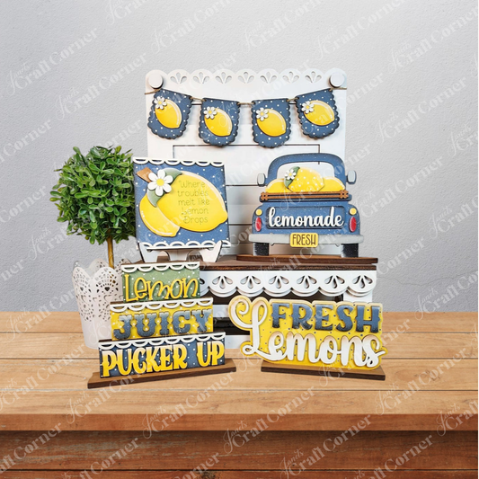 The Lemon Decor Set by Janet's Craft Corner includes farmhouse accents: lemon-themed signs (“Fresh Lemons,” “Lemon Juice,” “Pucker Up”), a faux potted plant, and a blue lemonade car cutout—perfect for charming DIY home decor.