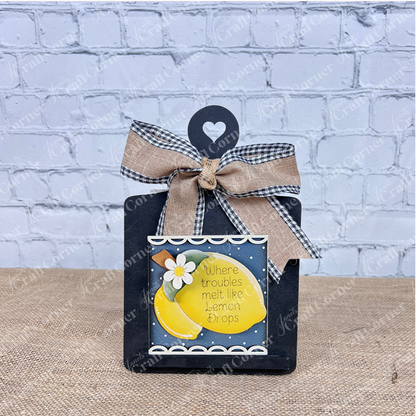Janet's Craft Corner's Lemon Squares is a decorative black plaque with a burlap and checkered bow, featuring a lemon-themed Swappable Squares card that says "Where troubles melt like lemon drops"—perfect for seasonal home décor.
