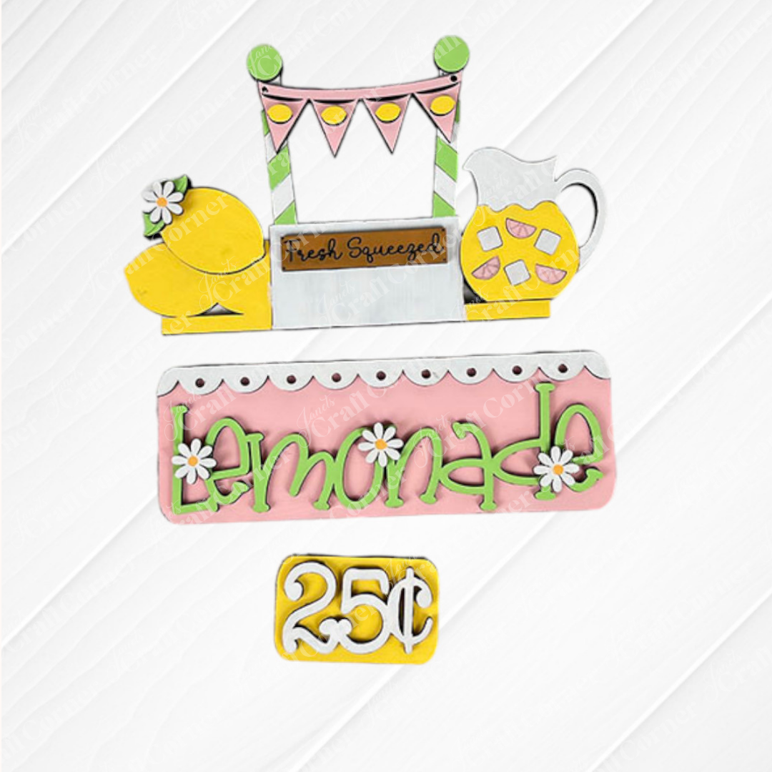 The "Lemonade Interchangeable Insert," part of Janet's Craft Corner DIY home decor kit, features vibrant cutouts of lemons, a pitcher, and a banner. Ideal for enhancing your living space, it sits on a textured white background that mimics embossed tin.