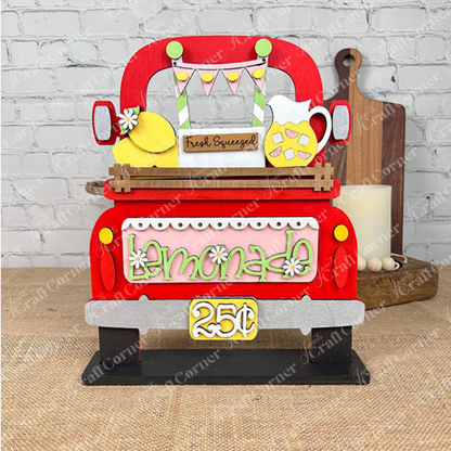 The Lemonade Interchangeable Insert DIY home decor kit by Janet's Craft Corner includes a charming hand-painted wooden display featuring a red truck with a "lemonade" sign priced at 25 cents. It comes complete with a lemon, pitcher, and "Fresh Squeezed" banner set against a brick wall backdrop, making it an ideal choice for home décor or as an interchangeable insert.