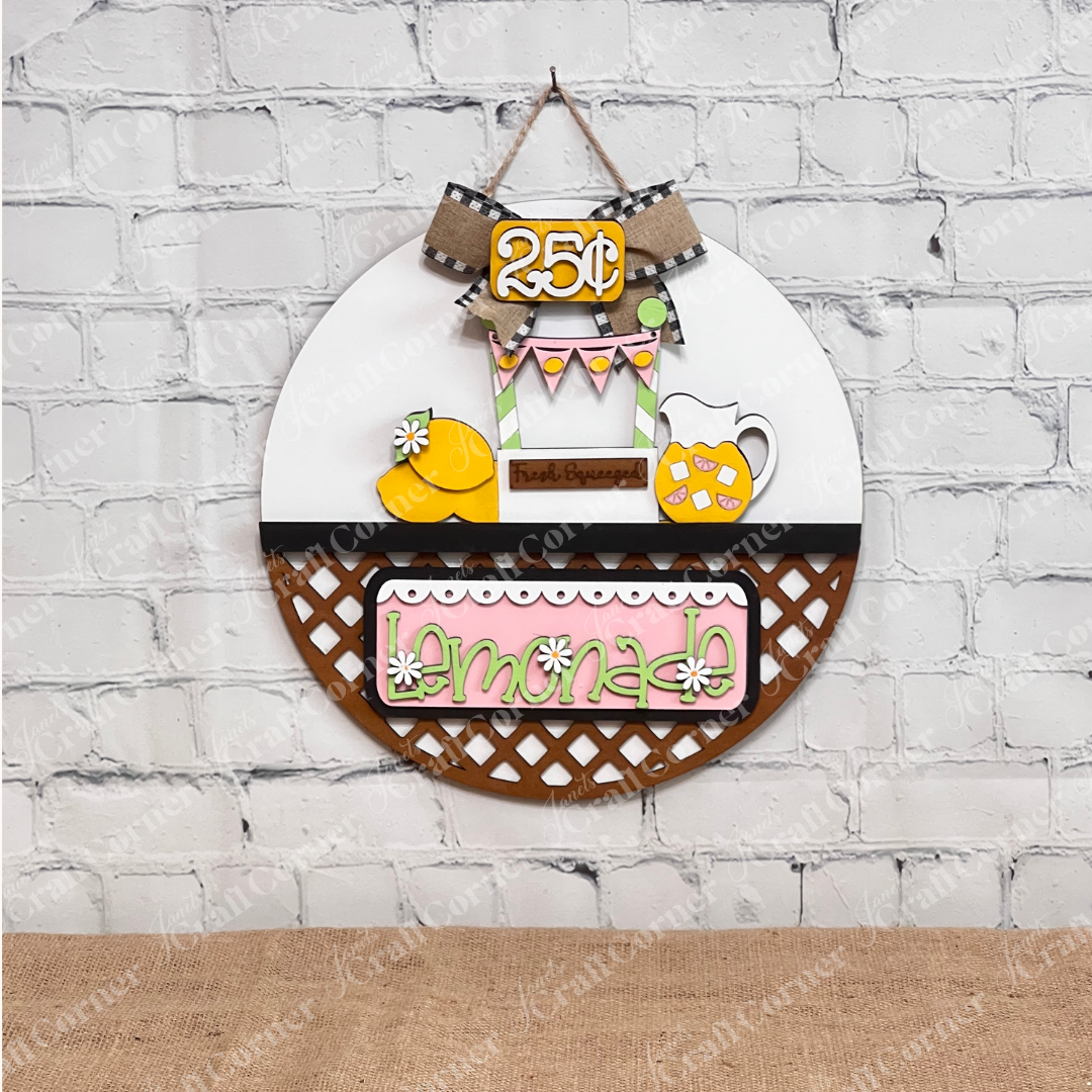 Janet's Craft Corner presents the Lemonade Interchangeable Insert, a delightful round door hanger DIY home decor kit. Featuring a lemonade theme with a pitcher of refreshing lemonade, fresh lemons, and a "Fresh Squeezed" sign, it's topped with a charming burlap and checkered ribbon bow. This hand-painted craft kit is perfect for any season due to its interchangeable insert feature.