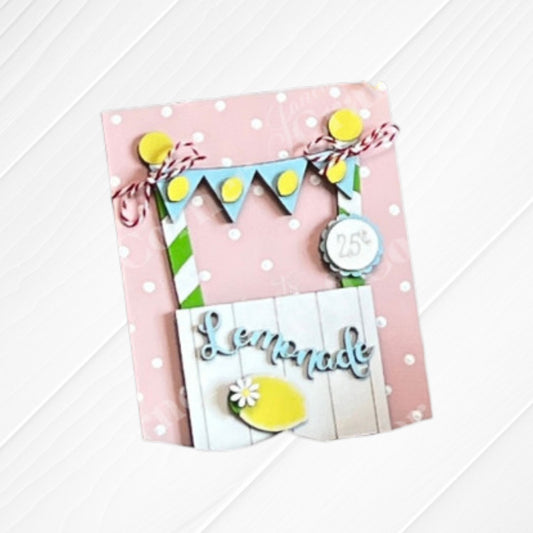 Janet's Craft Corner presents the Summer Switchable Farmhouse Signs – Painted: a handmade card with a lemonade stand, "25¢" sign, blue and yellow bunting, lemon cutout on white wood, and a pink polka dot backdrop for a charming summer touch.