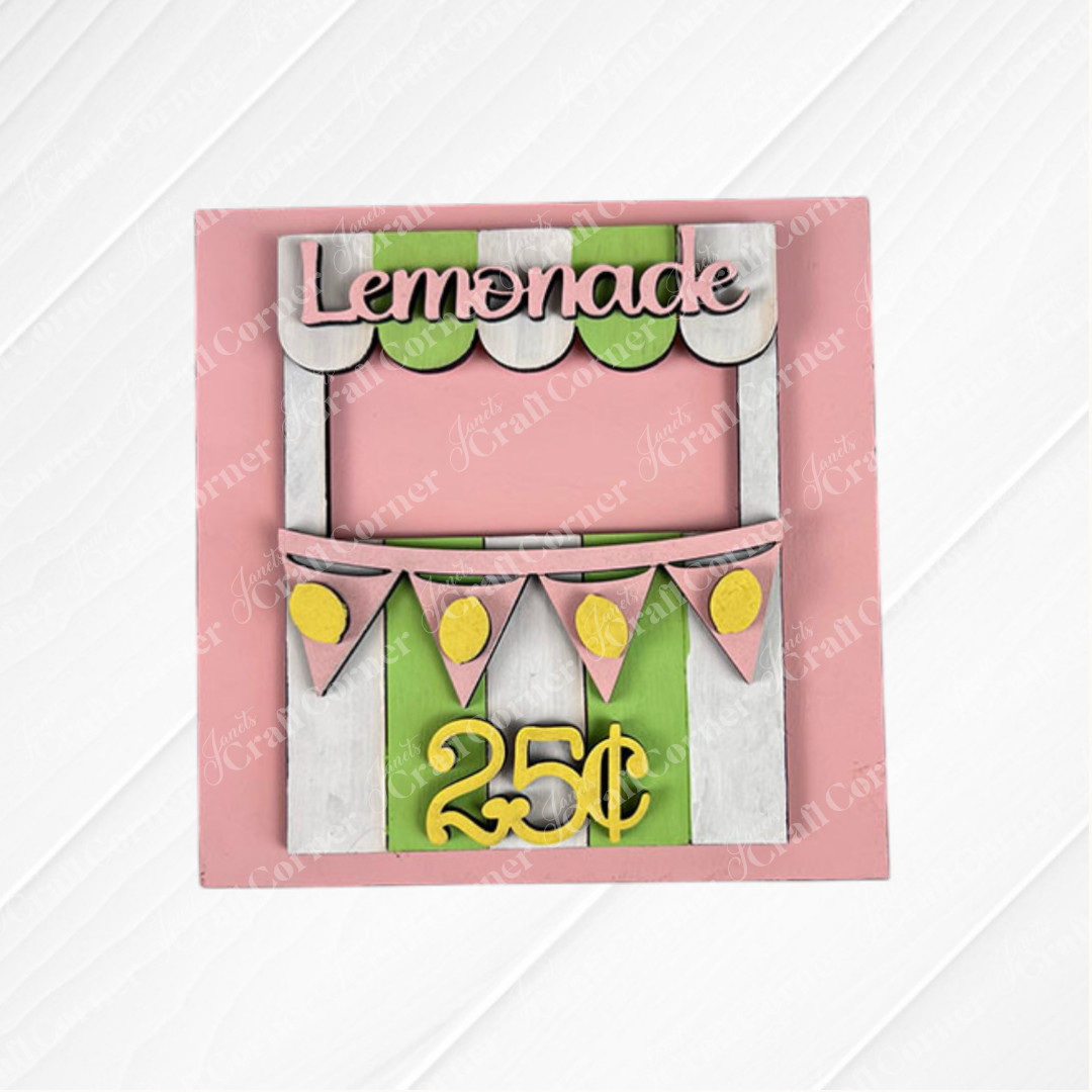 A vibrant Lemon Squares sign from Janet's Craft Corner features a pink background, green and white striped booth, yellow bunting, and "Lemon Squares" on top. Perfect for DIY decor or paired with Swappable Squares. Lemon Squares: 25 cents.