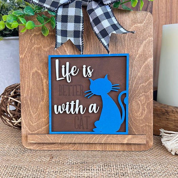 Janet's Craft Corner Cat Swappable Squares features a wooden sign with a blue cat silhouette, “Life is better with a cat,” wood cut-outs, black and white ribbon, greenery—perfect DIY rustic home decor.