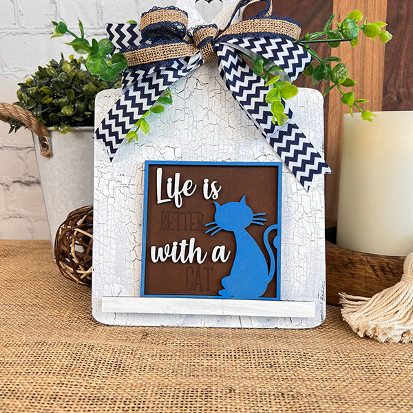 The Cat Swappable Squares by Janet's Craft Corner features a blue cat silhouette and "Life is better with a cat" text, perfect for tiered trays, accented with a chevron bow and green leaves for rustic decor.