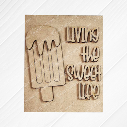 The Summer Switchable Farmhouse Signs kit by Janet's Craft Corner features a light wood plaque with a popsicle outline and "LIVING THE SWEET LIFE" in bold font—ideal rustic DIY decor for your farmhouse signs collection. Set of 1.
