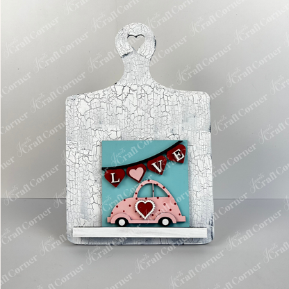 Janet's Craft Corner Valentine Squares features a white crackled board with a heart cutout, showcasing a teal square with a pink car, hearts, and "LOVE" garland—ideal tiered tray decor or for DIY Valentine's home projects.