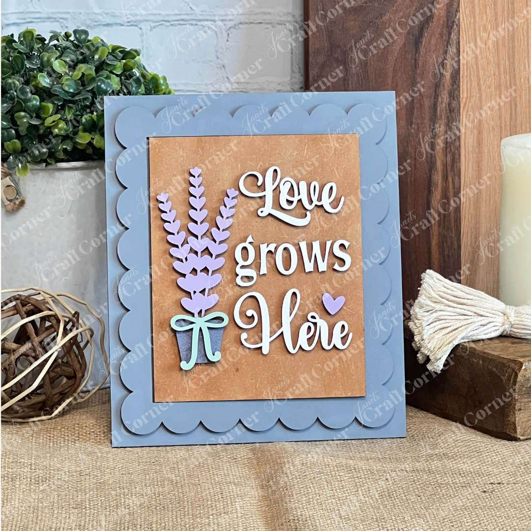 The Lavender Switchable Farmhouse Signs DIY Craft Kit by Janet's Craft Corner features a "Love grows here" sign with lavender flowers, a bow, and scalloped gray frame—perfect tiered tray décor for rustic table setups.