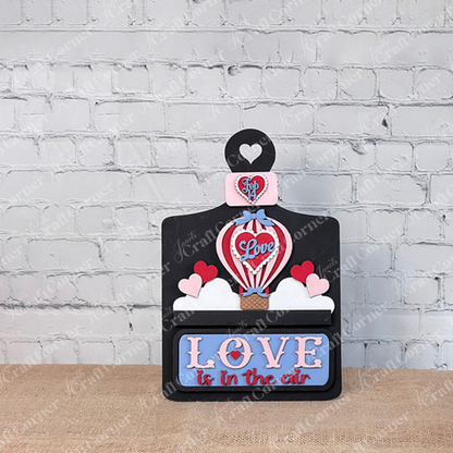 This whimsical "Love is in the Air" insert from Janet's Craft Corner showcases a hot air balloon with "Love" and hearts, with the phrase in pink and blue on white brick, elegantly set on rustic burlap.