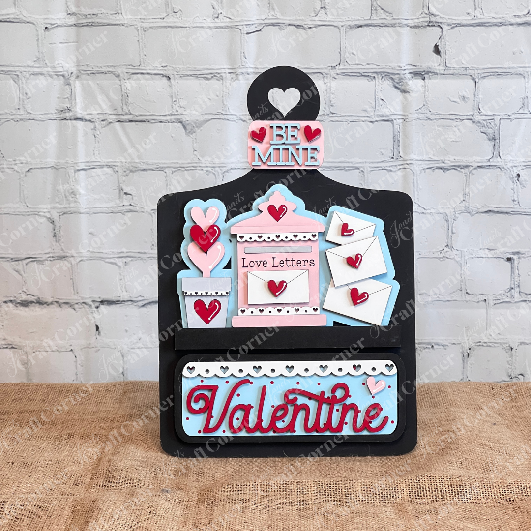 Janet's Craft Corner offers the "Love Letters Interchangeable Insert," a DIY decor kit perfect for Valentine's Day. It features three decorative pieces with "Be Mine," "Love Letters," and "Valentine" scripts, adorned with hearts and envelopes against a rustic backdrop for personalized inserts.