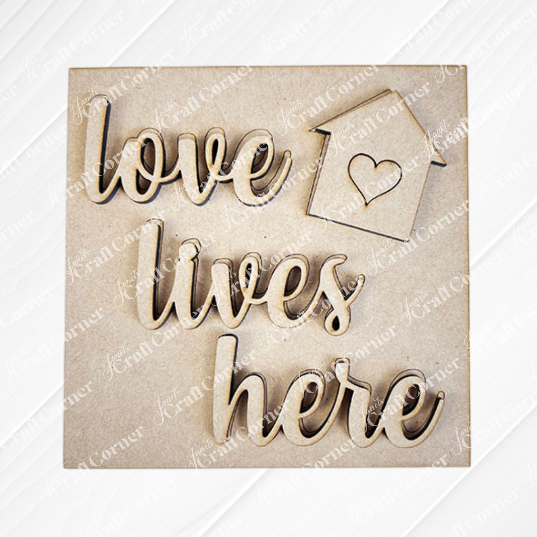 The Home Squares sign by Janet's Craft Corner features cursive "love lives here" text and a small house with a heart, making it perfect for tiered tray decor. Displayed on a neutral background.
