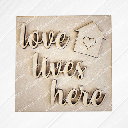 The Home Squares sign by Janet's Craft Corner features cursive "love lives here" text and a small house with a heart, making it perfect for tiered tray decor. Displayed on a neutral background.