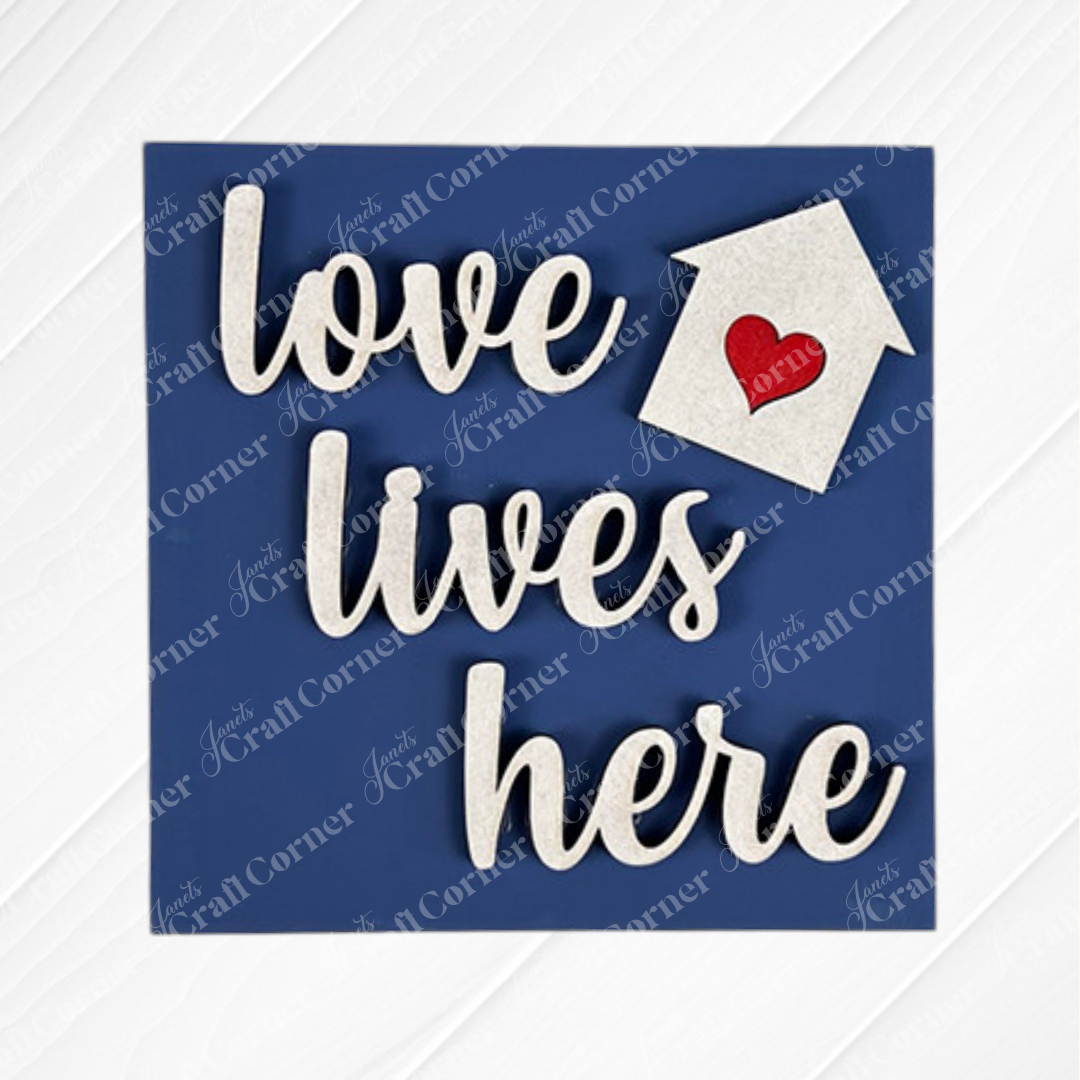 The Home Squares sign by Janet's Craft Corner features blue square design, white cursive "love lives here" text, a small white house with a red heart, and subtle diagonal texture—perfect for tiered tray decor.