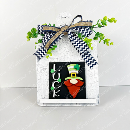 Janet's Craft Corner's Lucky Irish Squares is a house-shaped decorative sign with a green-hatted gnome, "LUCK" wood cut-outs, a chevron bow with greenery, and cracked white paint—ideal for tiered tray displays.