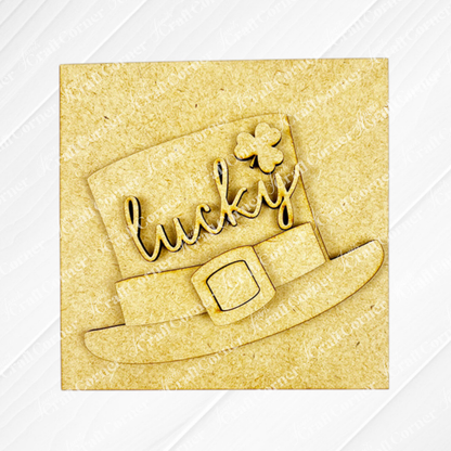 The Lucky Irish Squares by Janet's Craft Corner feature a wooden leprechaun hat cutout with "lucky" and a four-leaf clover, ideal for tiered tray decor, shown on a light textured background.