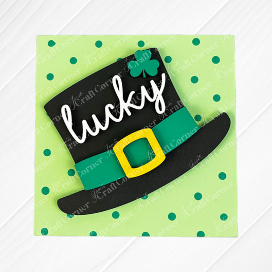 Janet's Craft Corner's Lucky Irish Squares features a black top hat with a green band, yellow buckle, shamrock, and "lucky" in white script on a light green polka dot background—perfect for tiered tray decor.