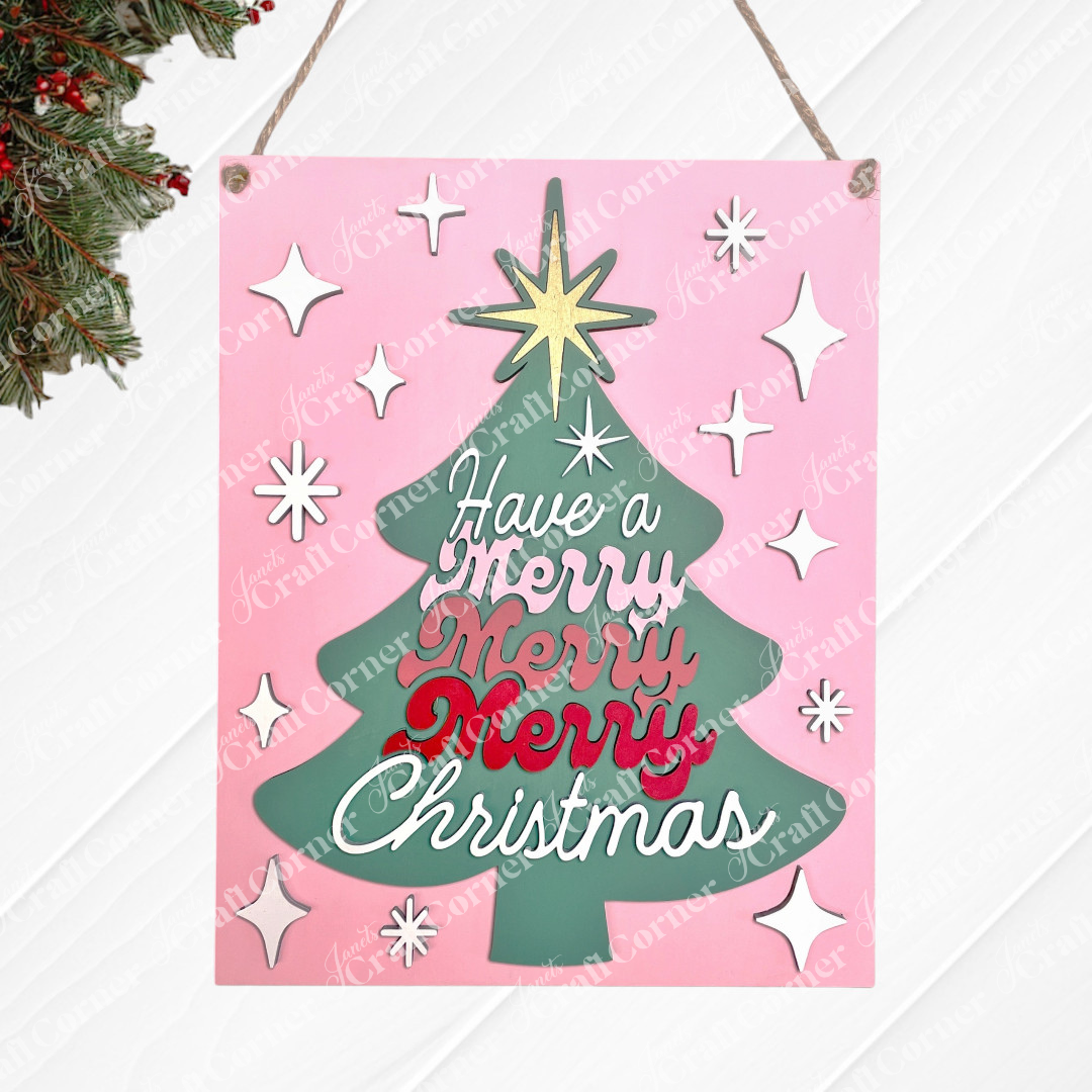Janet's Craft Corner "Have a Merry Christmas Tree" Wall Hanger is a DIY seasonal home decor craft kit featuring a green tree shape on a pink background with white stars and "Have a Merry Merry Merry Christmas" in red and white script. Set of 1.