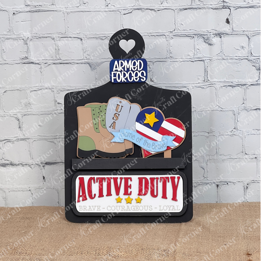 Janet's Craft Corner presents the Military Interchangeable Insert—a DIY home decor kit featuring stylized military boots, USA dog tags, and a medal. A heart reads "ARMED FORCES," while burlap-textured text states "ACTIVE DUTY" and "BRAVE - COURAGEOUS - LOYAL.