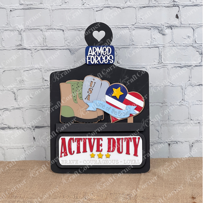 Janet's Craft Corner presents the Military Interchangeable Insert—a DIY home decor kit featuring stylized military boots, USA dog tags, and a medal. A heart reads "ARMED FORCES," while burlap-textured text states "ACTIVE DUTY" and "BRAVE - COURAGEOUS - LOYAL.