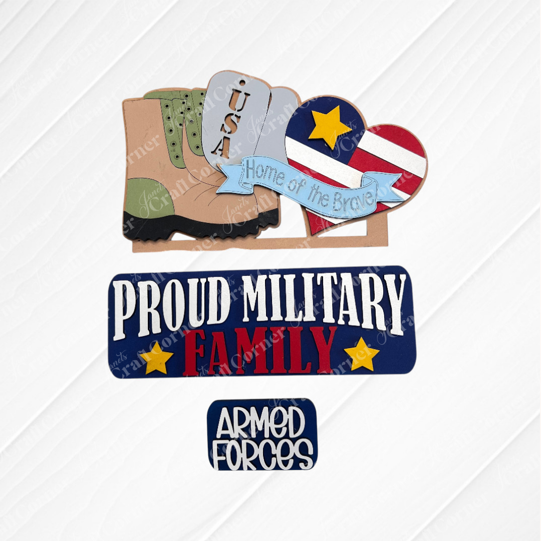 The Military Interchangeable Insert by Janet's Craft Corner features a boot, "USA" dog tags, a heart with stars and stripes, the text "Home of the Brave," and plaques reading "Proud Military Family" and "Armed Forces." Ideal for interchangeable home decor or as a DIY hand-painted craft kit.