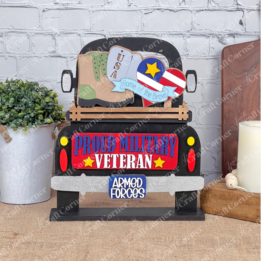 Introducing the Military Interchangeable Insert from Janet's Craft Corner, a DIY home decor kit that features decorative wooden artwork with a truck adorned with "Proud Military Veteran" and "Armed Forces" signs. This piece includes patriotic symbols such as a heart, star, and boots labeled with "USA," along with the inspiring text "Home of the Brave." It's an ideal choice for interchangeable home decor, beautifully displayed against a brick wall alongside a plant and candle.