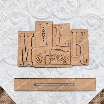 The Milk & Honey Mini Word Block by Janet's Craft Corner is a DIY seasonal home decor craft kit. It features wooden cutout letters on a wooden block background with a rectangular wooden slot for customization.