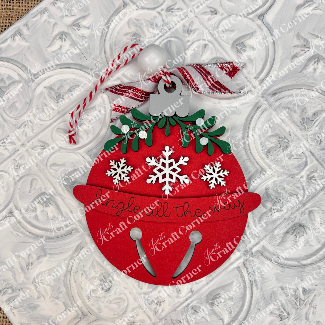 The Mistletoe Ornaments DIY Decor Kit by Janet's Craft Corner, set of 6, lets you craft festive ornaments with red bells, white snowflakes, green leaves, striped ribbons, and "Jingle all the way" displayed on a textured white surface.
